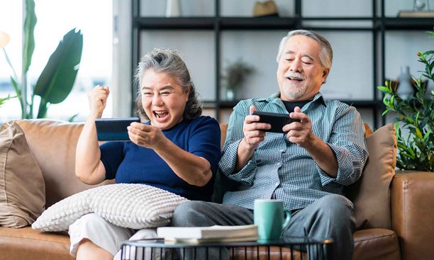 Elderly couple sitting on the sofa cheering at something they are looking at on thier phones