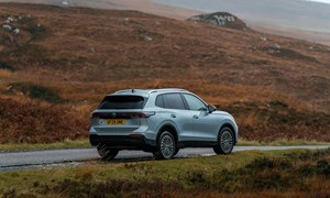 a grey car with a UK licence plate drives on a scenic road