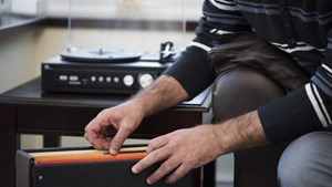 Man going through LPs next to a record player at home