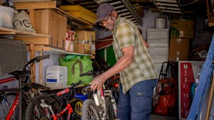 an elderly man tidies away bicycles in a garden shed