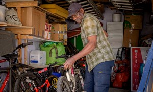 an elderly man tidies away bicycles in a garden shed
