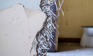 A broken wall with loose fill insulation coming out, which contains asbestos