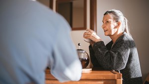 a woman in a grey cardigan drinking coffee at a table in discussion with another person