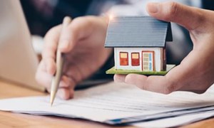 Person reviewing documents on a desk and holding a model house