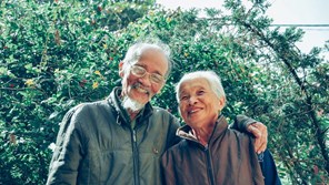 an elderly asian couple smile and hug in a gardening centre